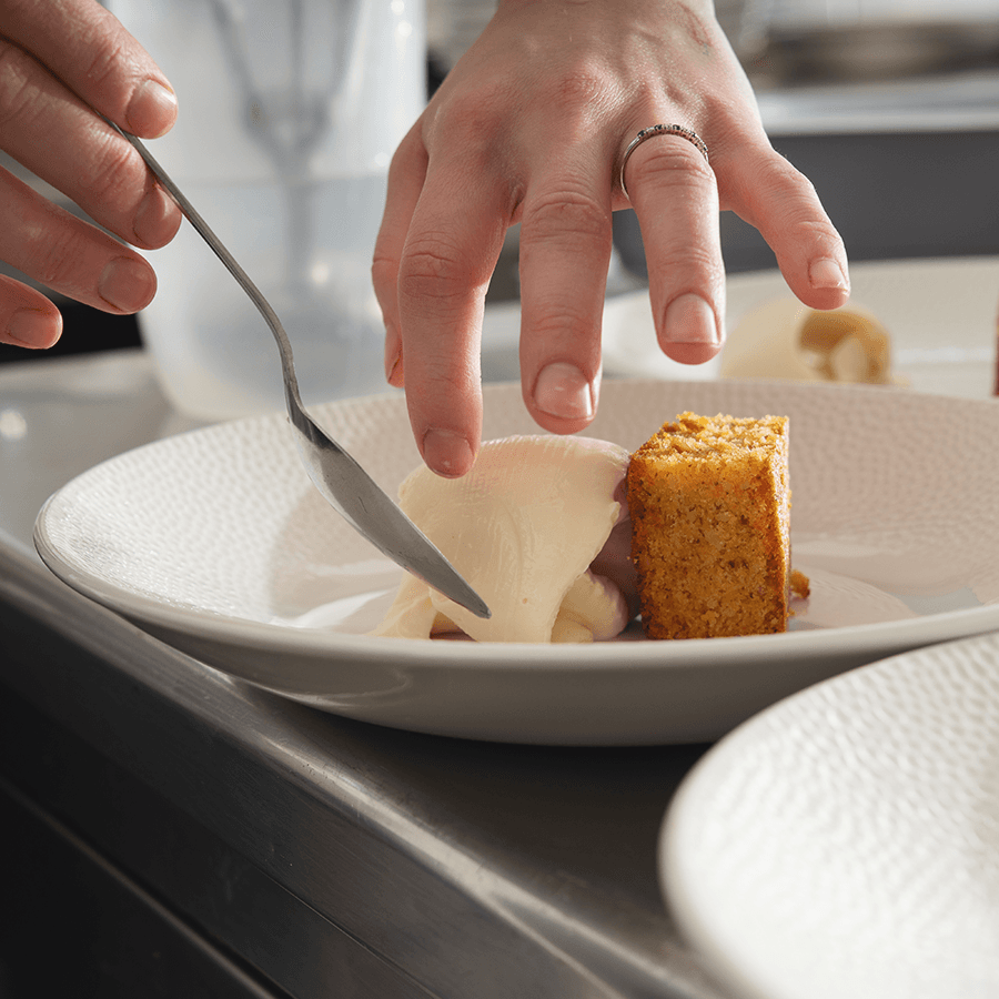 Una mano posa il cucchiaio accanto a una fetta di torta con crema, sul piatto appena impiattato
