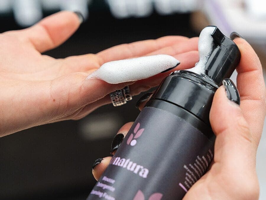 Una mano preme l’erogatore del flacone nero e raccoglie sulle dita una nuvola di mousse bianca