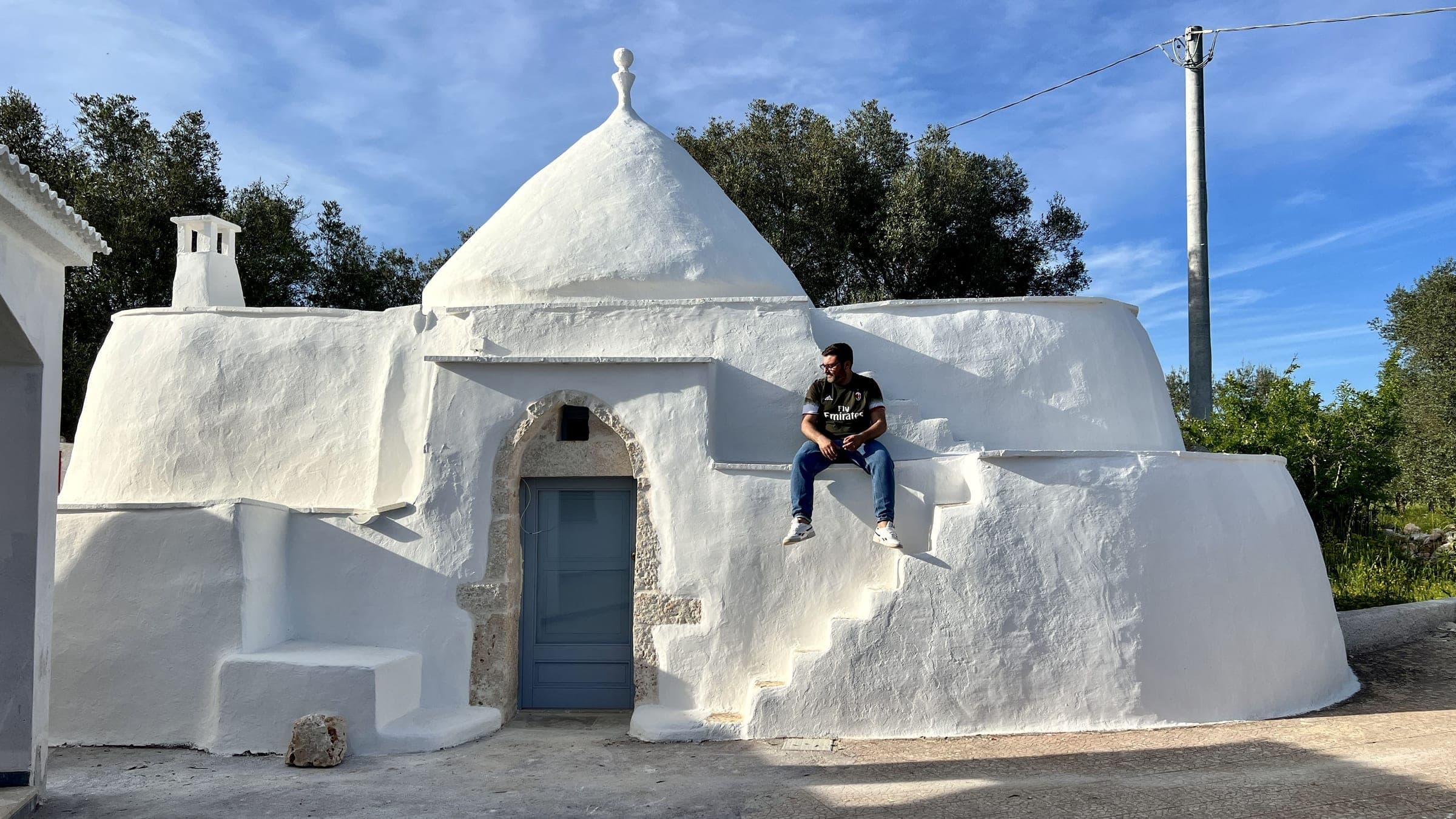 Una persona seduta sul muro bianco del Trullo Giggino, sotto un cielo azzurro