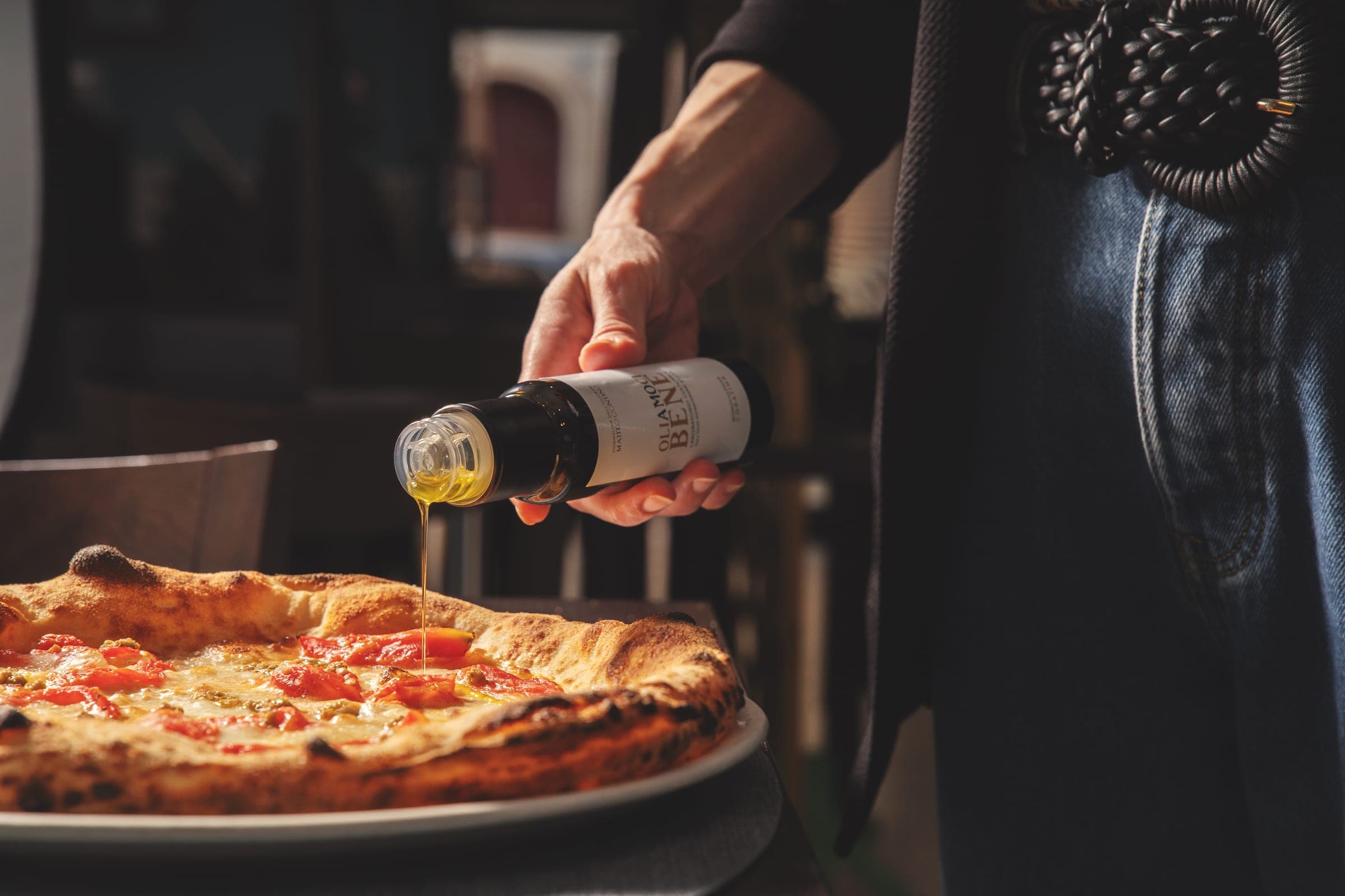 Un filo d'Olio EVO versato da una bottiglia su una pizza appena sfornata