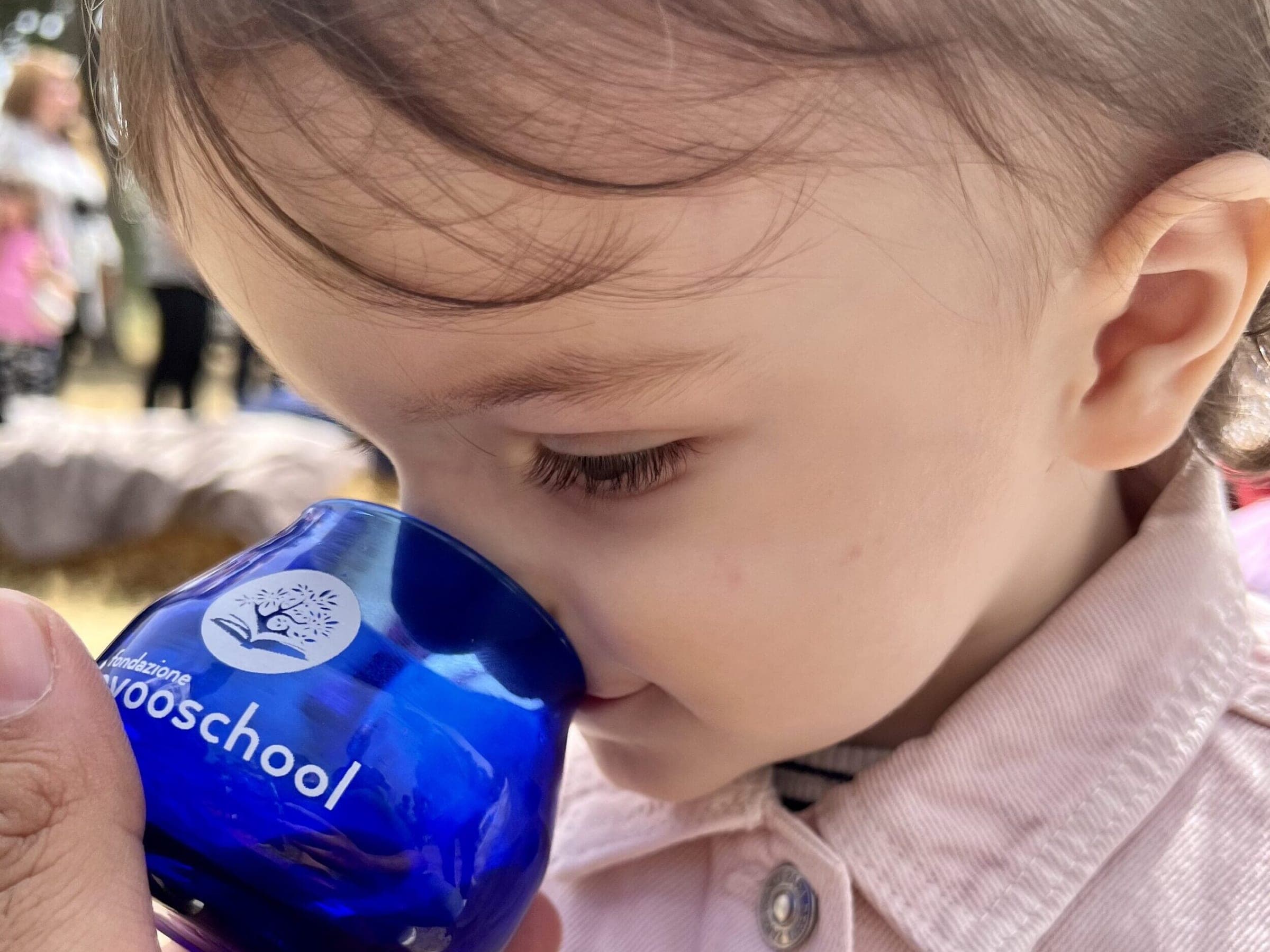 Una bambina annusa l’olio in un bicchiere blu della Fondazione Evoo School, tenuto da una mano adulta