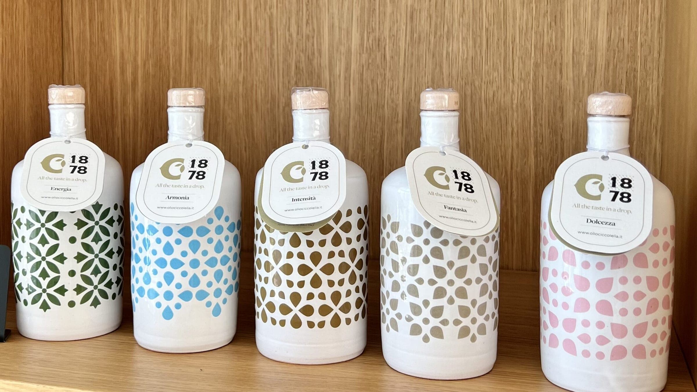 Cinque bottiglie di ceramica bianca con decori verdi, azzurri, dorati, grigi e rosa su uno scaffale di legno